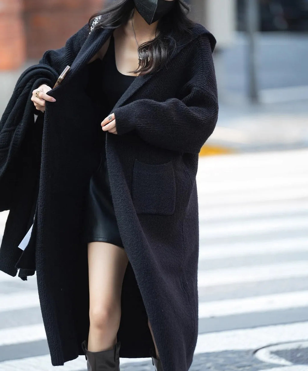 Long grey knitted women's cardigan with a hood, styled like a trench coat, on a hanger.