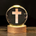 White crystal ball ornament on a wooden warm light base, showing engraved religious symbols.