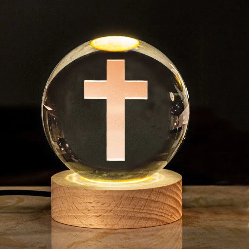 White crystal ball ornament on a wooden warm light base, showing engraved religious symbols.