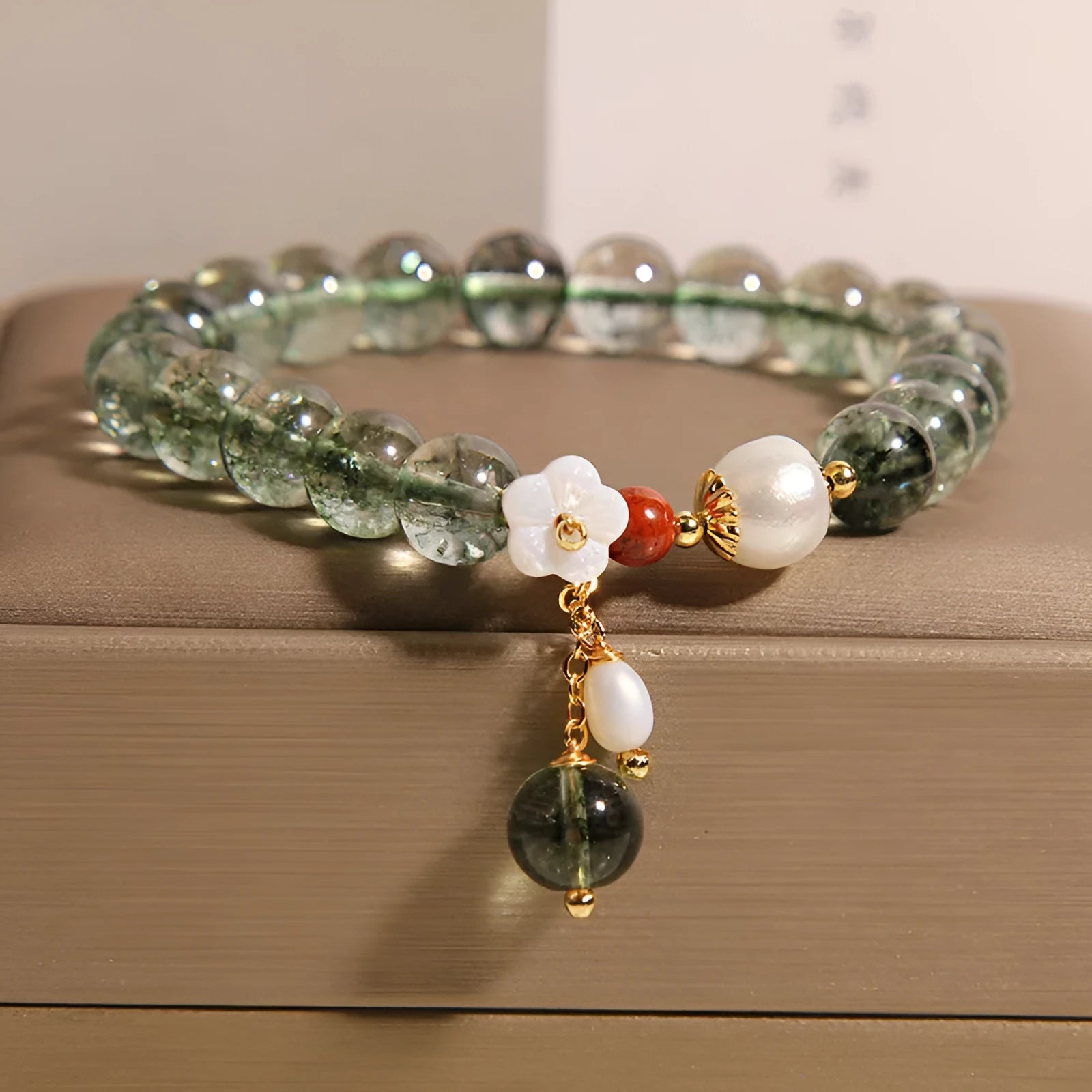 Green phantom quartz crystal bracelet with a silver shell flower charm on a model's wrist.