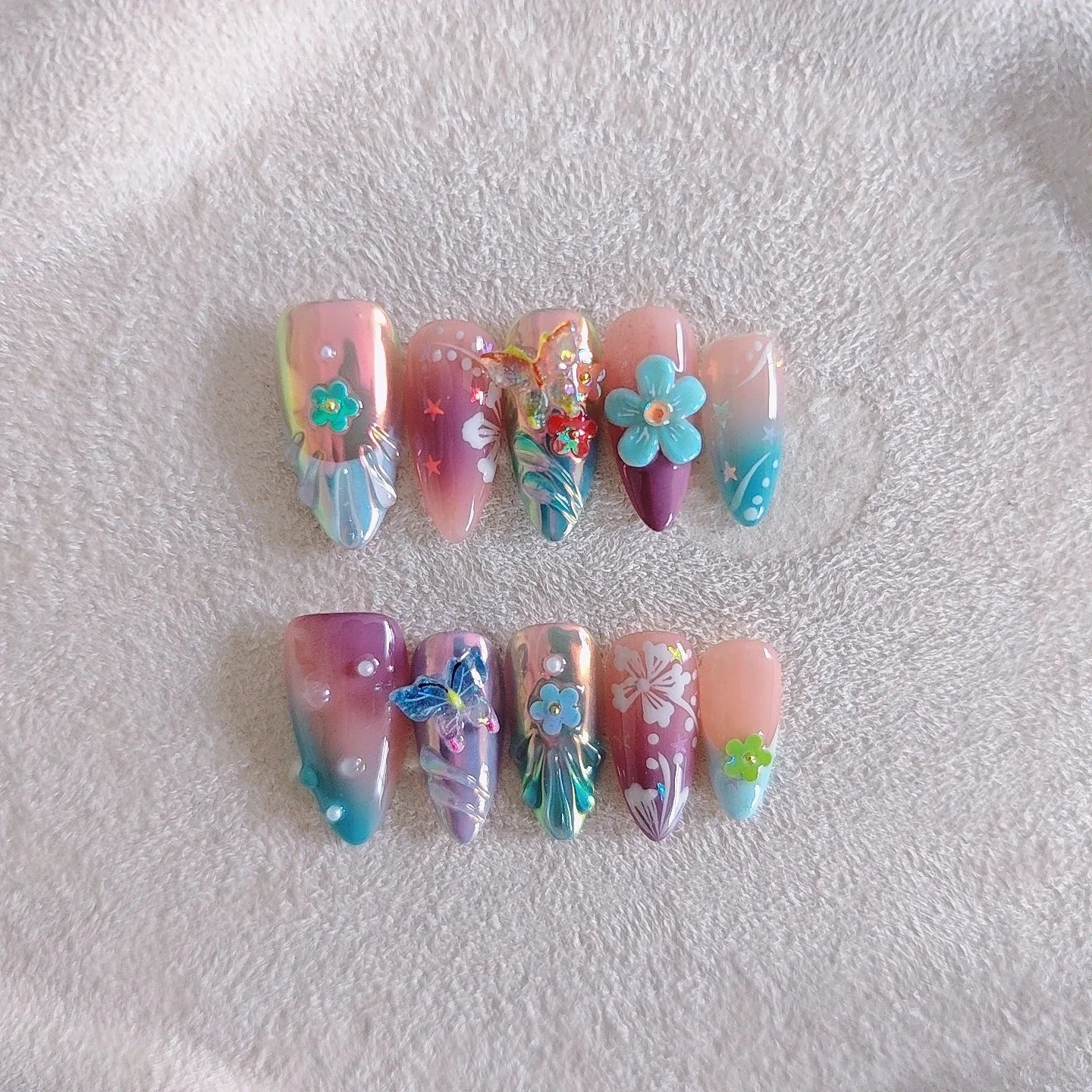 Handmade colourful false nails with 3D embossed flowers and butterflies on almond-shaped nails