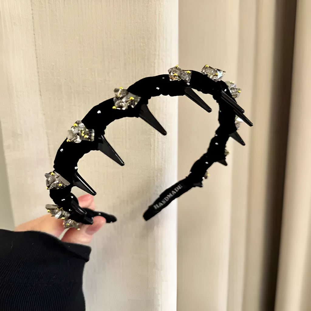 A wine red velvet hairband with a crystal wave decoration, sitting on a dark surface.