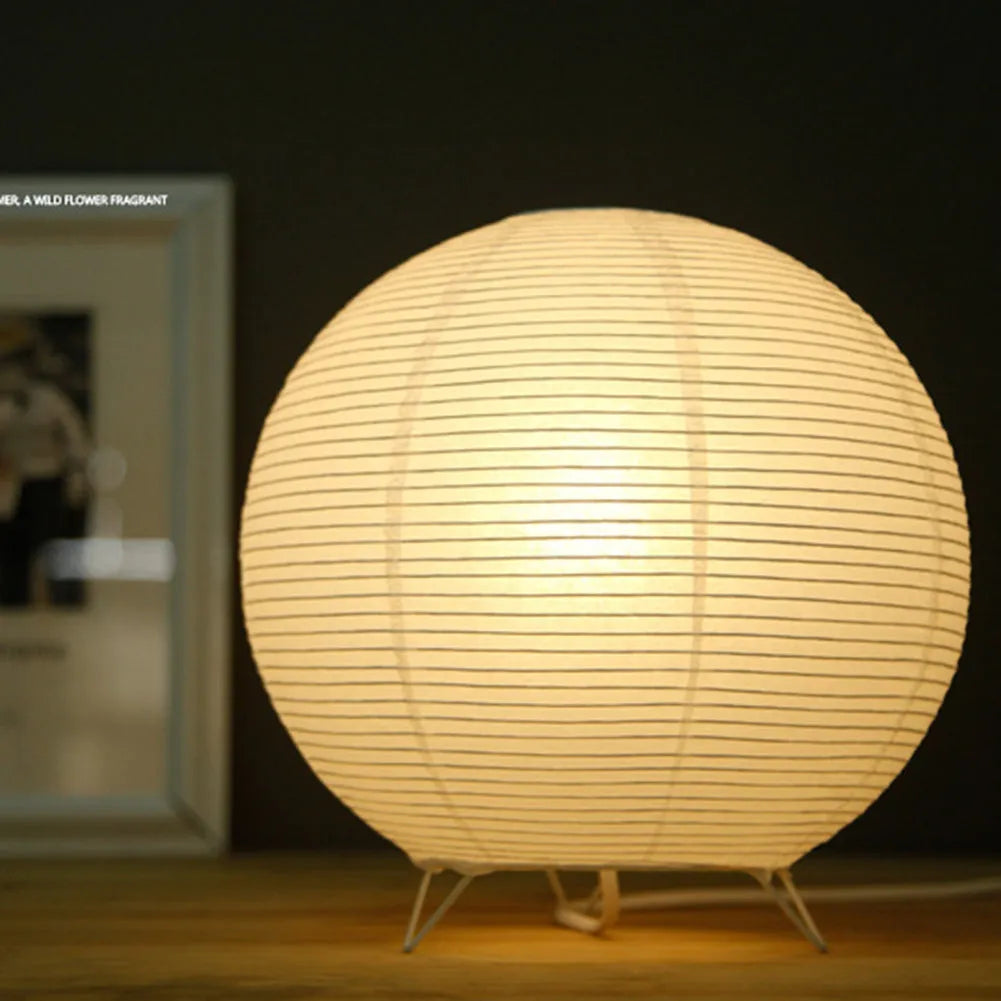 White rice paper plug-in table lamp in circular shape on a wooden bedside table.