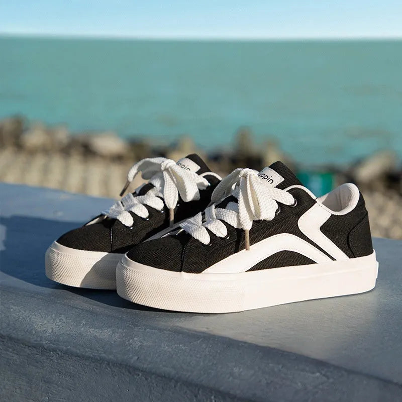 Women's low-top board shoes in a black and white colour combination, showing round toe and front lace-up design.
