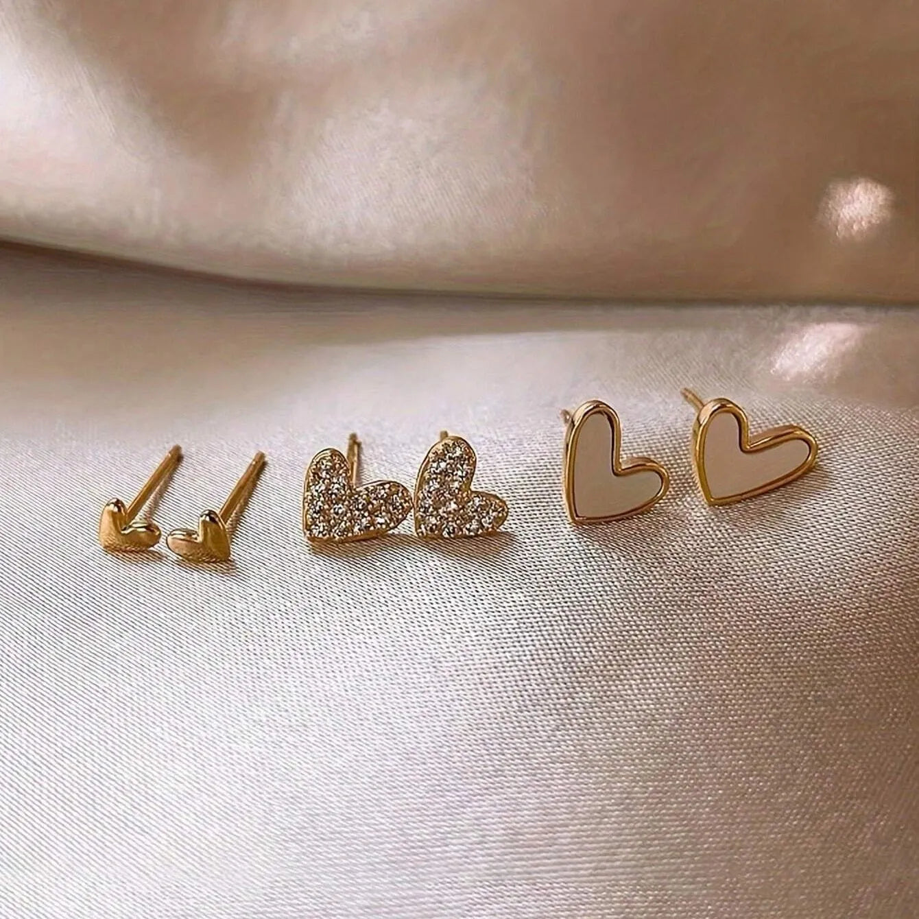 Set of three pairs of heart-shaped alloy earrings in gold, black, white, and pink colours.