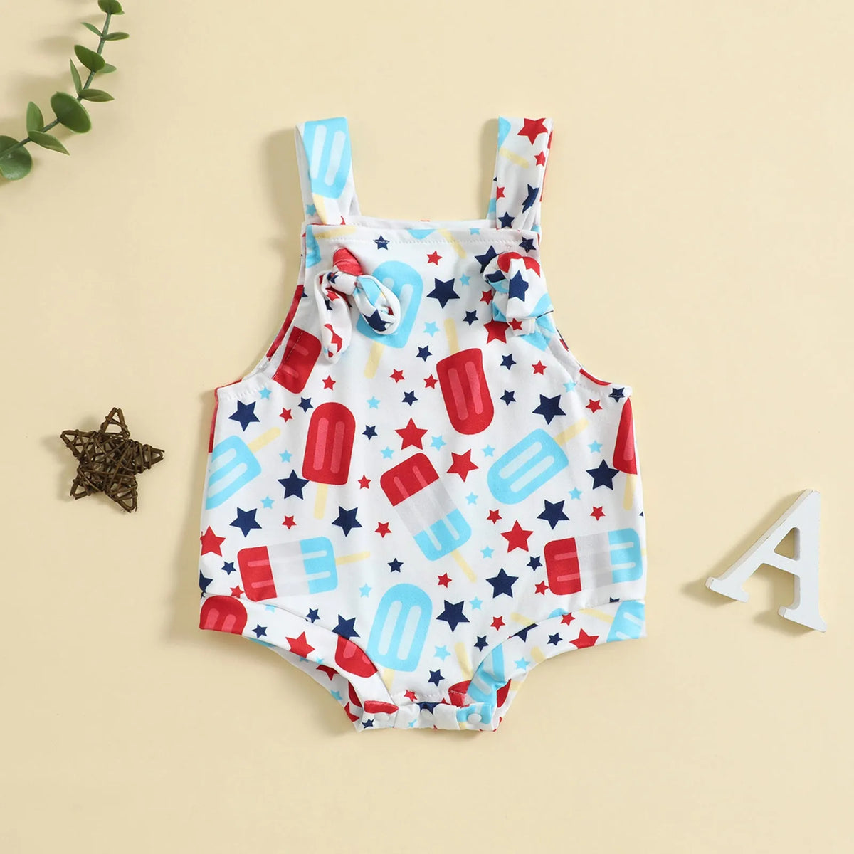 Baby girl wearing a sleeveless knotted front suspender pants jumpsuit in a printed design.