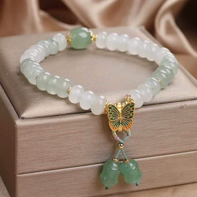 Green crystal abacus bead bracelet with a retro butterfly charm and tassels on a white background.