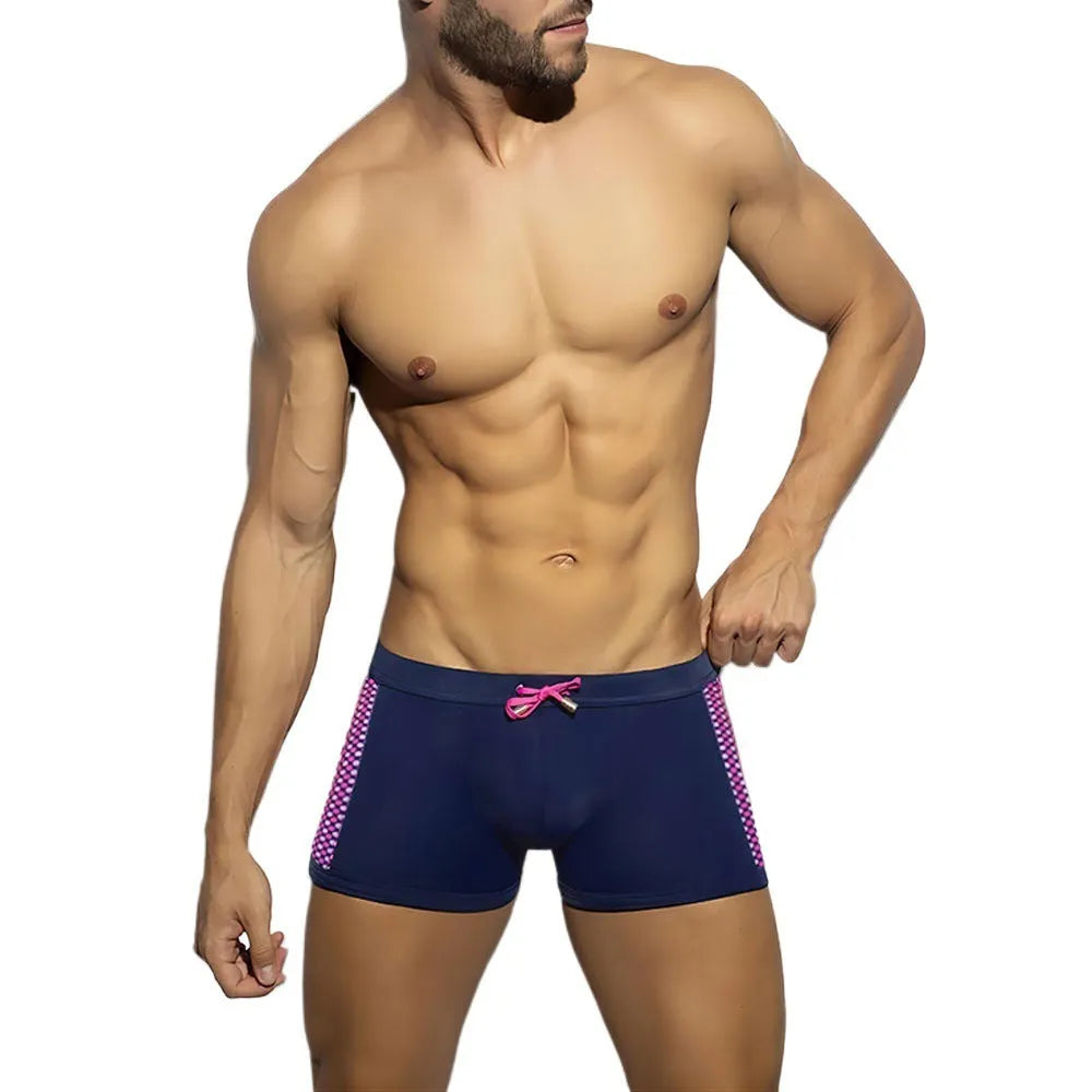Men's black polka dot swimming boxers with a dark blue ribbon trim on a grey background.