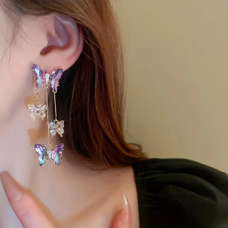 Women's silver needle coloured drop earrings with purple butterfly charm, crystal flowers, and tassels.