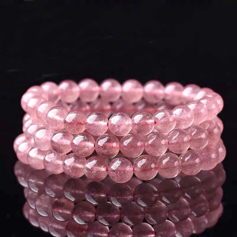 A women's bracelet with round, polished strawberry quartz crystal beads in pinkish-red tones.