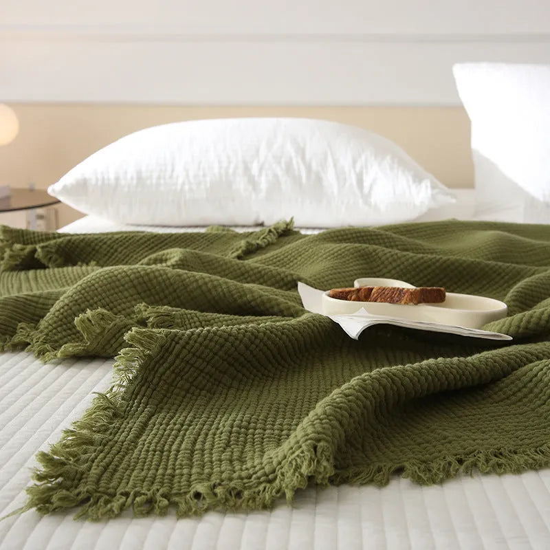 Soft cotton four-layer gauze throw blanket with tassel edges in navy blue, shown draped over a sofa.