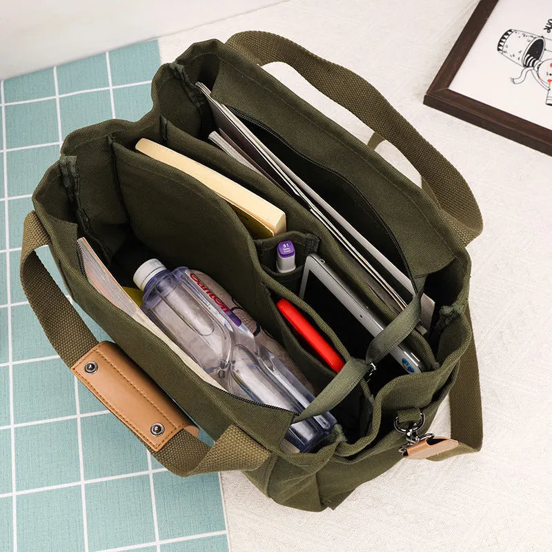 Horizontal square canvas tote bag in neutral colour with open zipper sides showing internal phone, document, computer and camera pockets