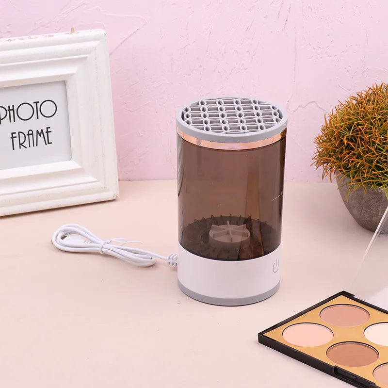 Grey and white electric makeup brush cleaner machine with USB cable on a white background