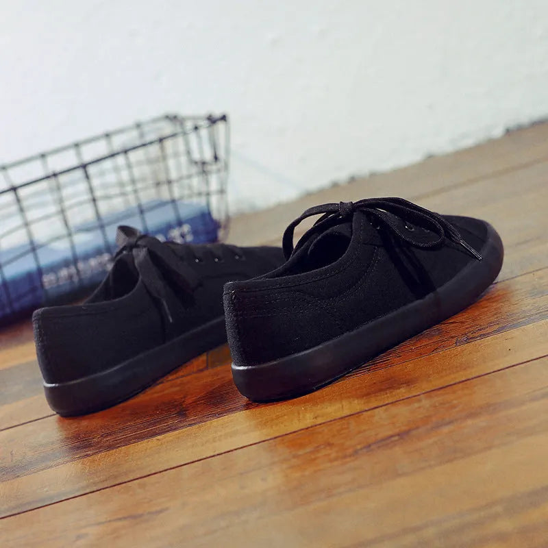 All black low top canvas lace-up shoes with a flat rubber sole for women.