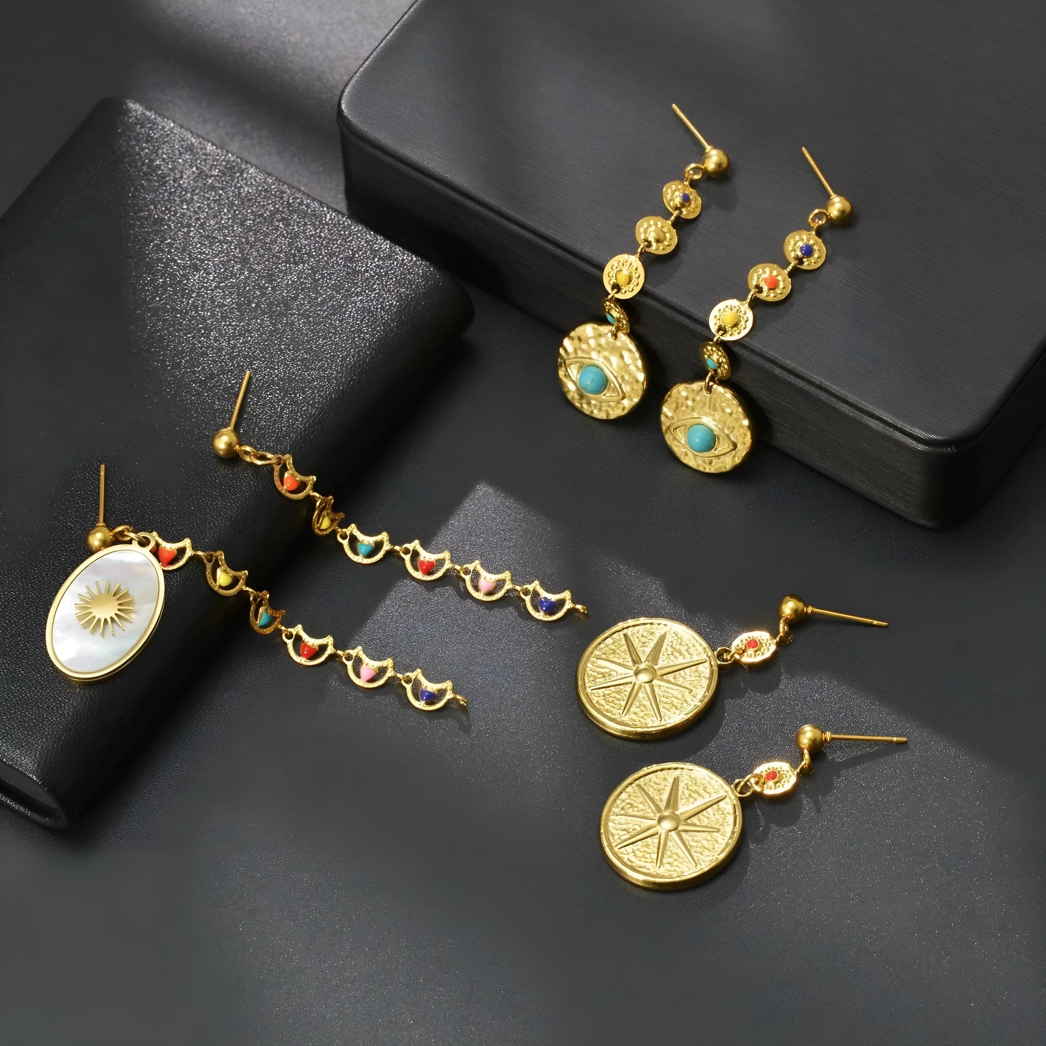 Three pairs of stainless steel geometry earrings: a star design, an eye design, and a shell sun design.