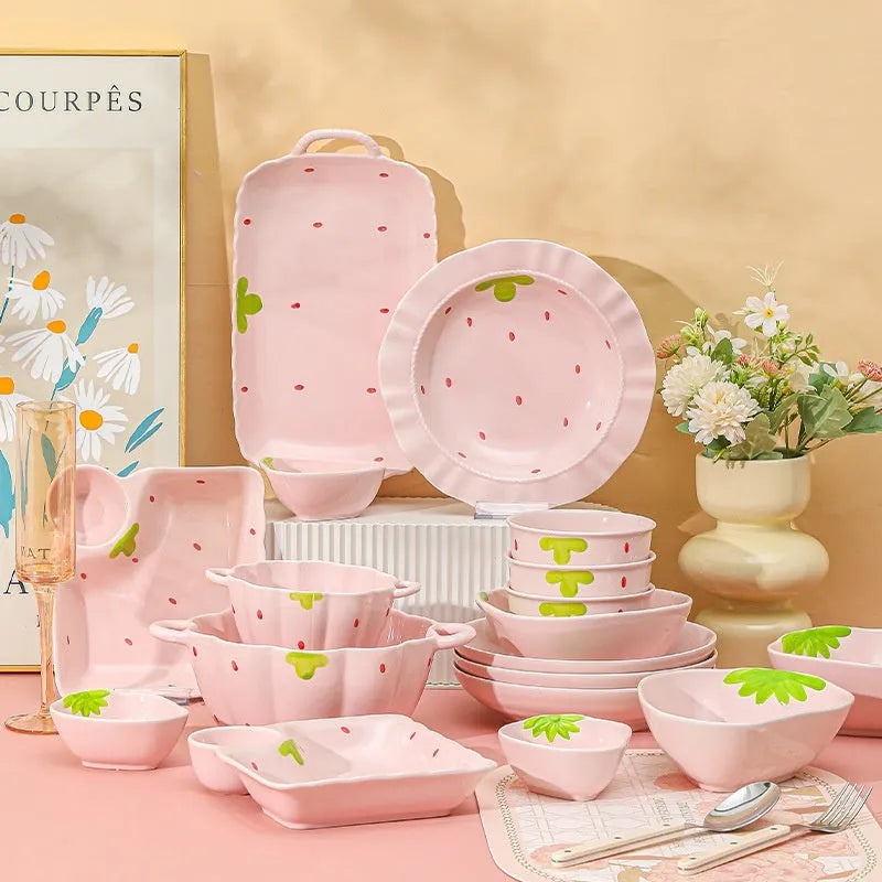 Cute strawberry pattern porcelain dinnerware set with plates, flower bowls, and a twist spoon on a table.