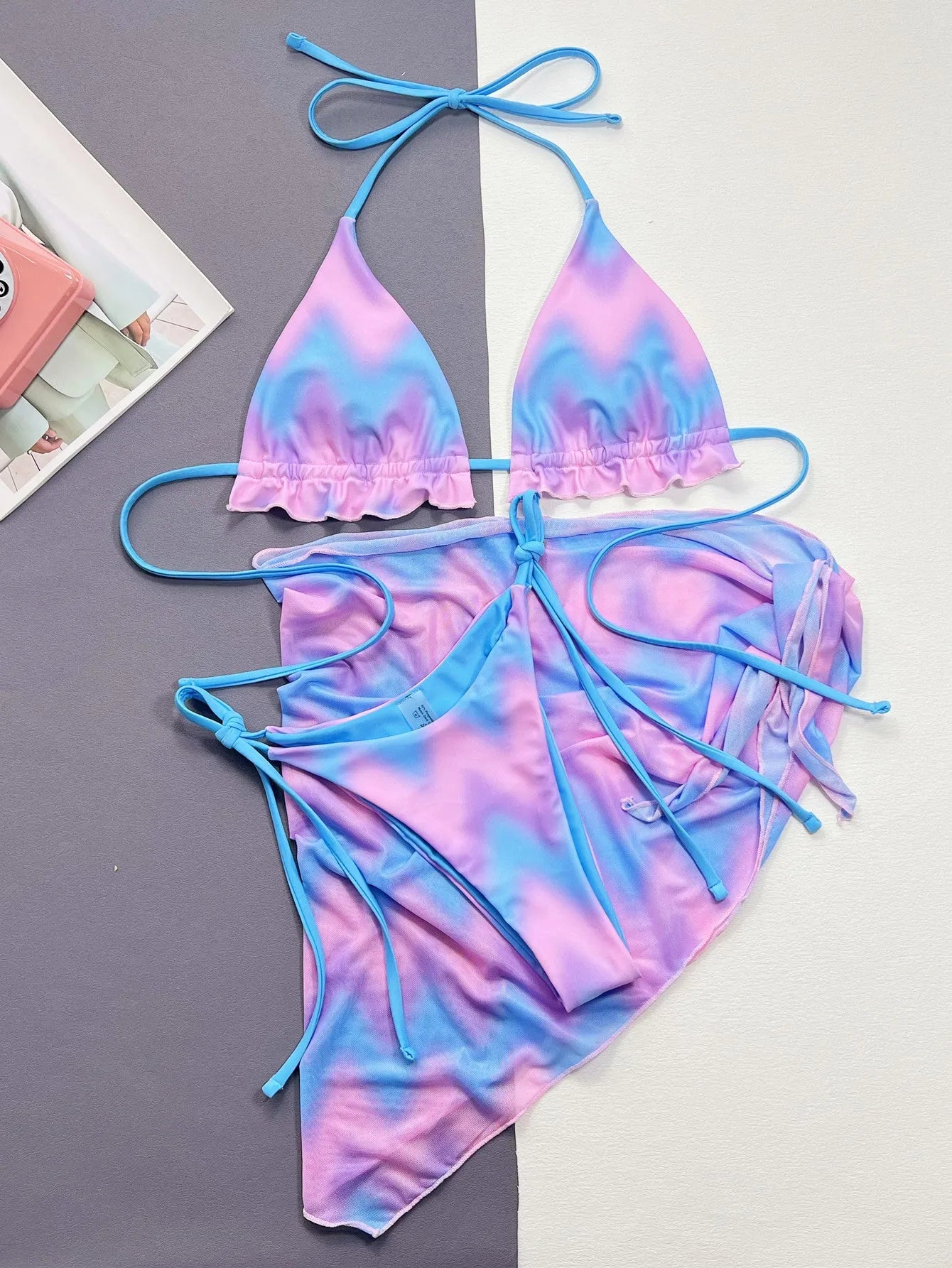Women's tie-dye pattern bikini set with matching skirt on a neutral background.