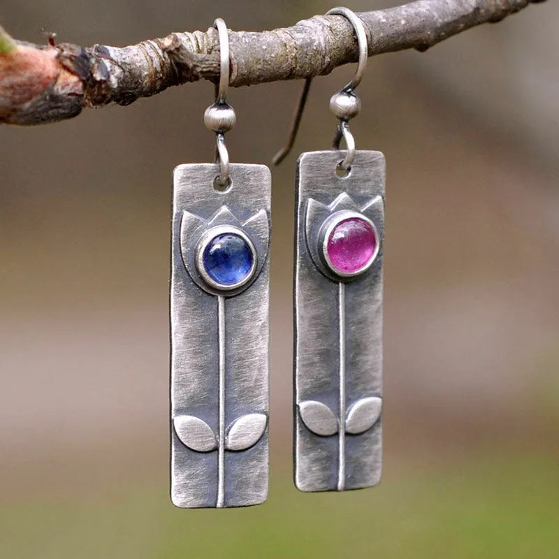 Antique finish red sapphire earrings with geometric shape and elliptical gemstone elements on metal background