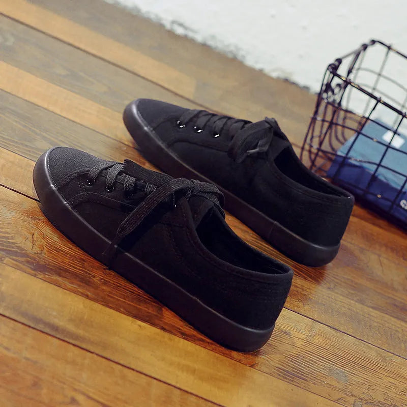 All black low top canvas lace-up shoes with a flat rubber sole for women.