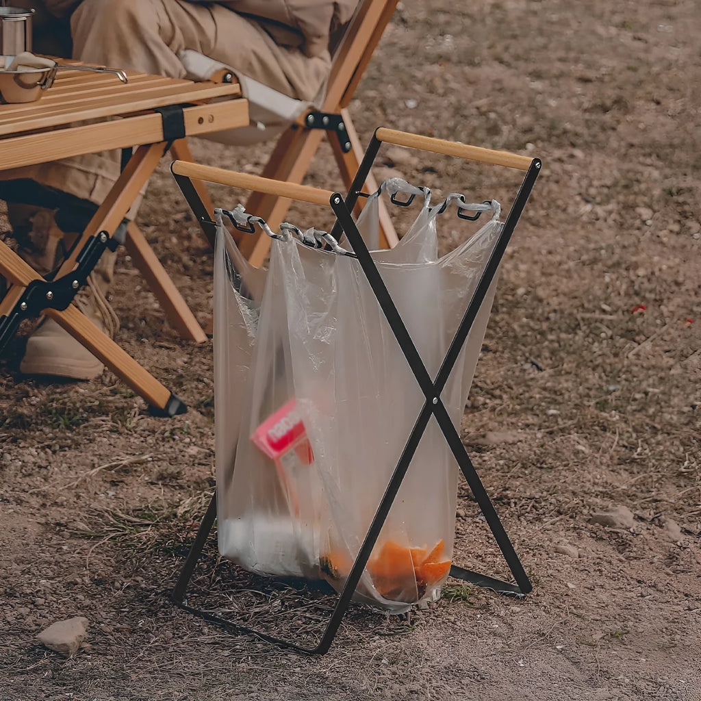 Foldable black wrought iron garbage storage hanger with a wooden handle, shown holding a bin bag.