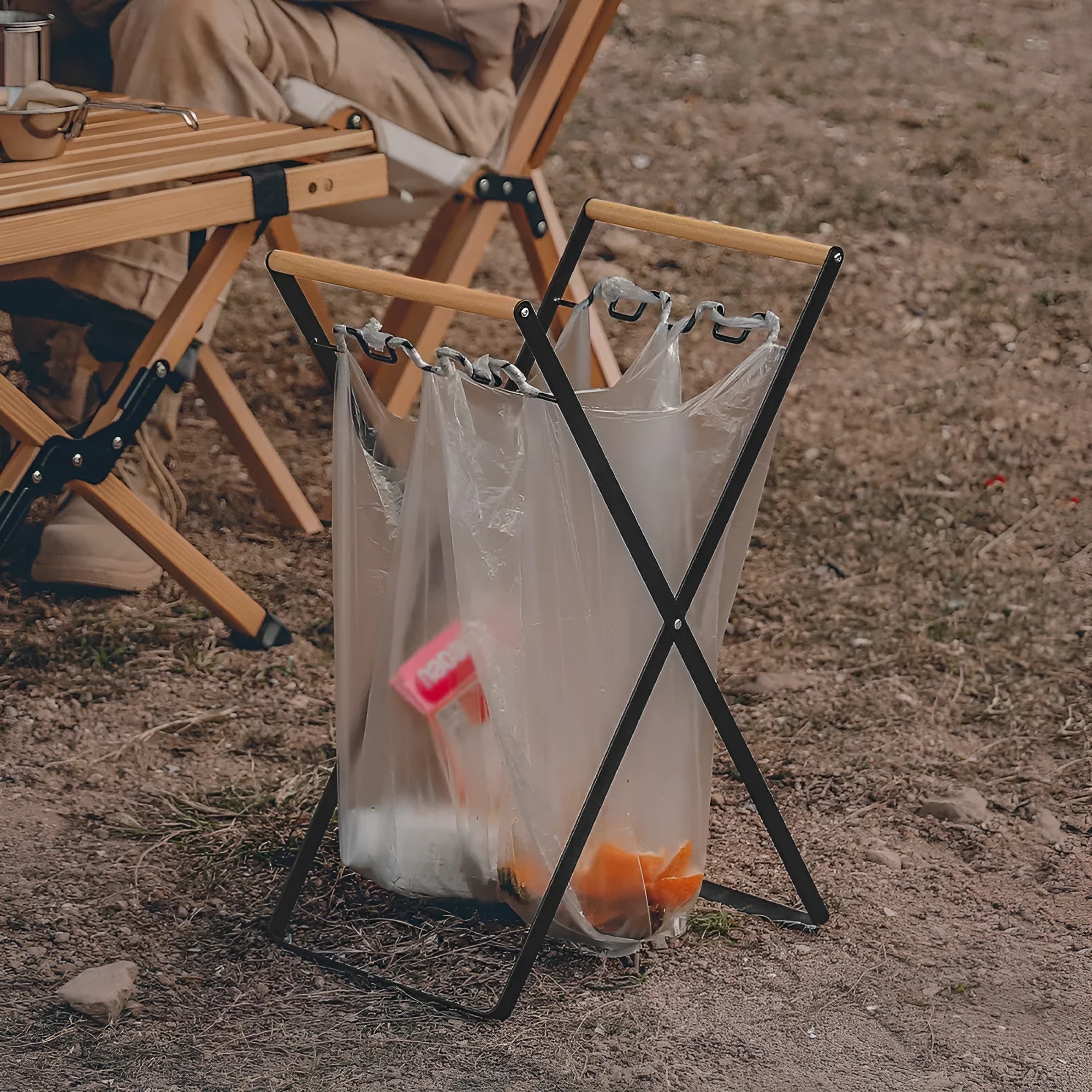 Foldable black wrought iron garbage storage hanger with a wooden handle, shown holding a bin bag.