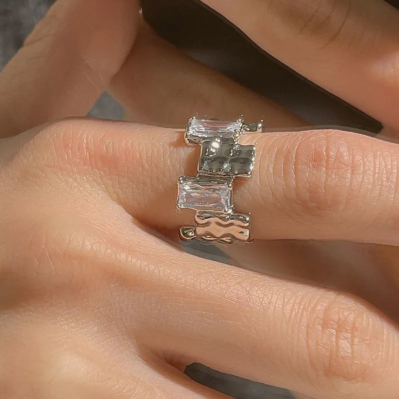 Silver plated open ring with a cross design and zircon gemstones in a geometric shape.