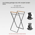 Foldable black wrought iron garbage storage hanger with a wooden handle, shown holding a bin bag.