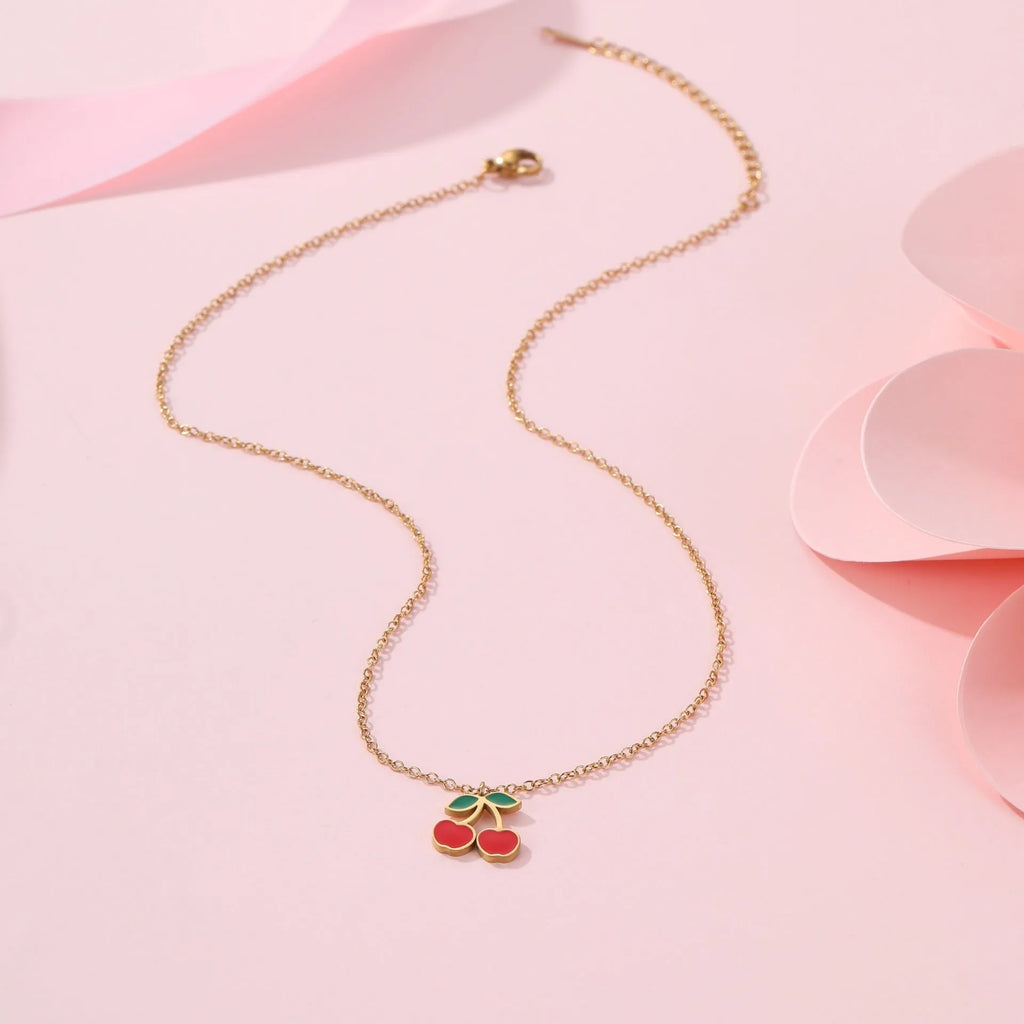 Cherry design jewellery set with gold plated necklace, bracelet, earrings, and ring on a flat surface.