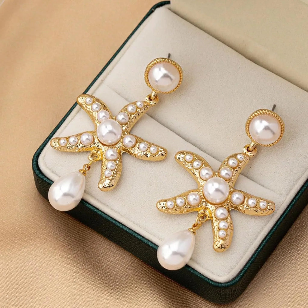 Women's gold-tone starfish drop earrings with a single off-white pearl centre on a light background