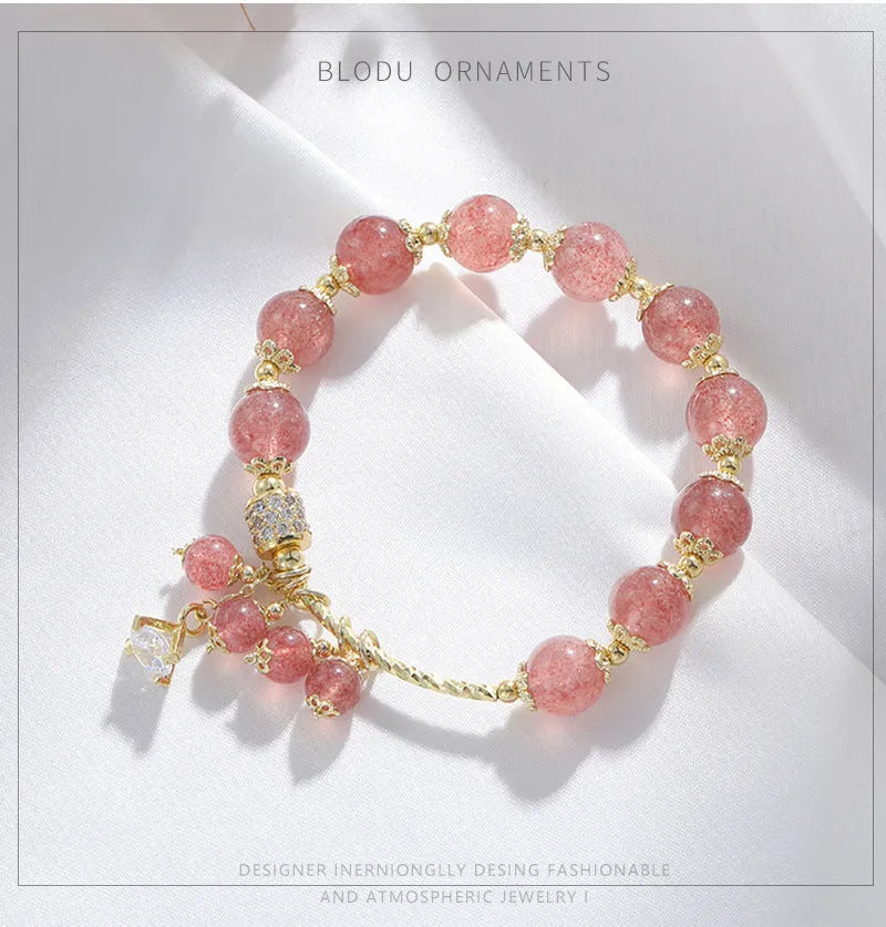 Close-up of a women's pink strawberry quartz crystal bracelet with heart-shaped beads and pearl accents.