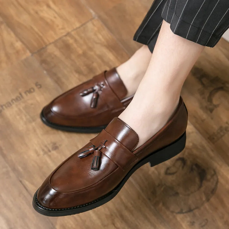 Men's black and brown slip-on business casual shoes with tassel detail and rubber sole.