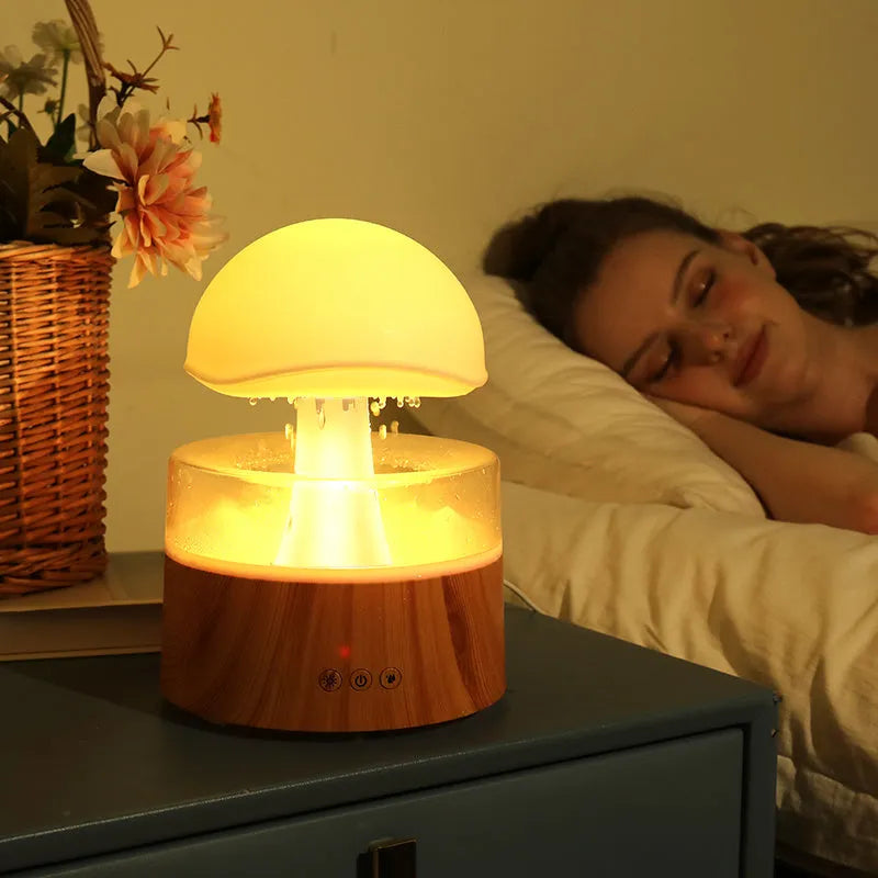 White cloud-shaped humidifier with falling raindrop mist and multi-colour night light on wooden table