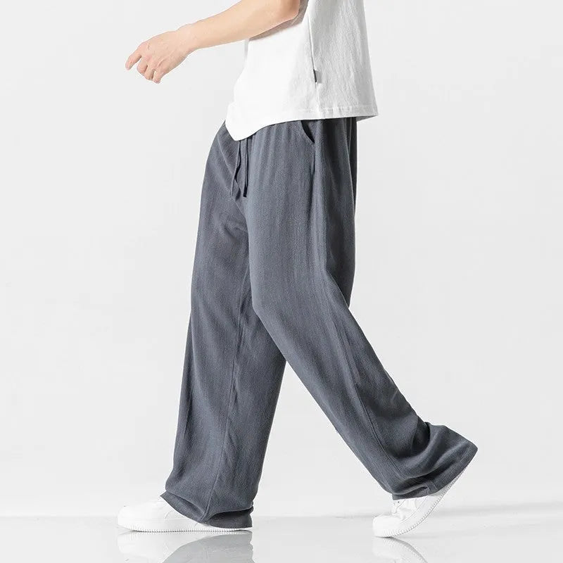 Man wearing beige straight-leg linen trousers with a drawstring waist, showcasing the cropped length and casual fit.