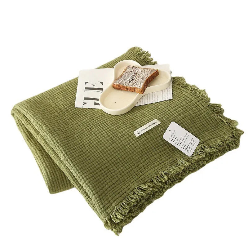 Soft cotton four-layer gauze throw blanket with tassel edges in navy blue, shown draped over a sofa.