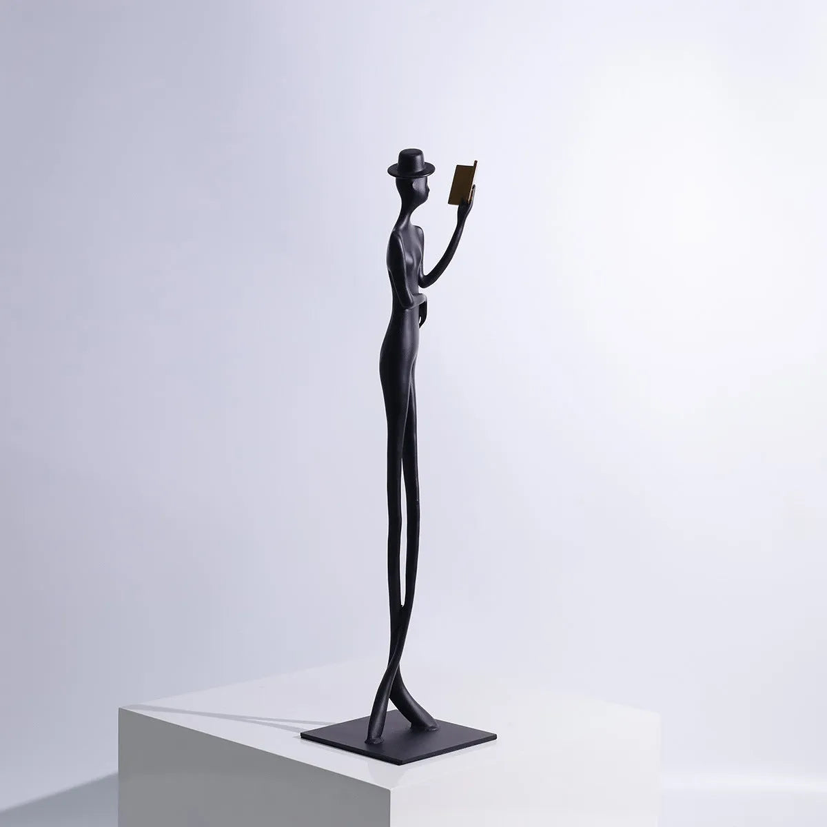Black metal sculpture of a woman reading, modern aluminium desktop ornament.