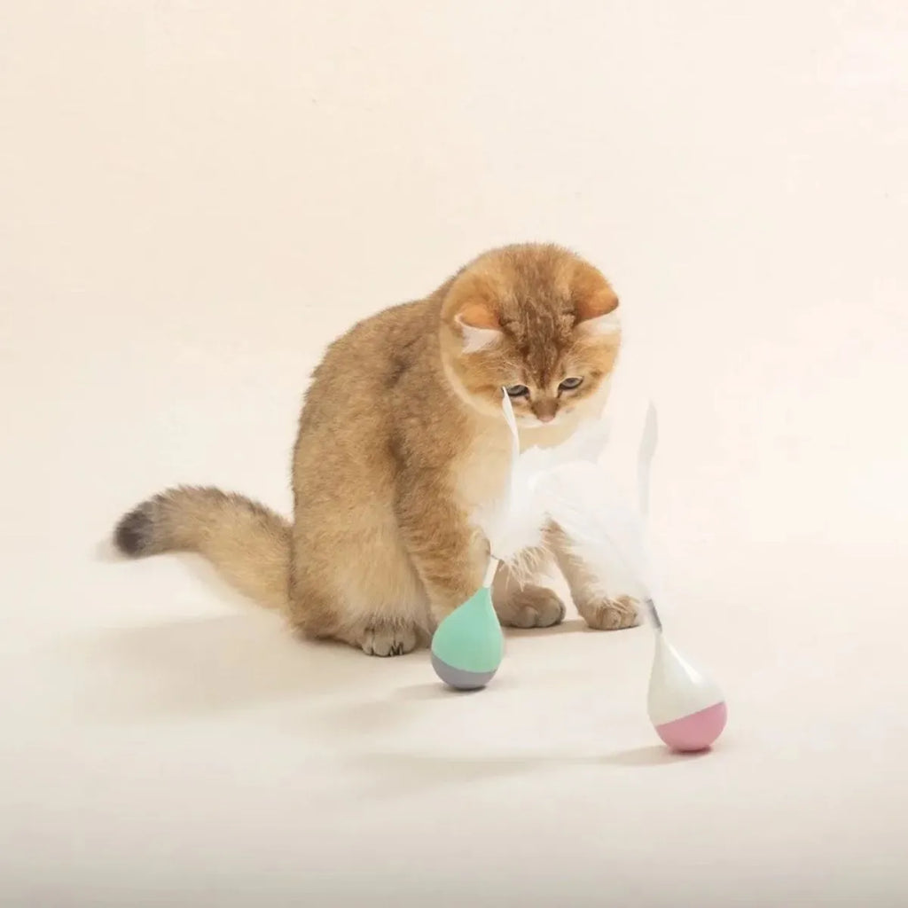 Green feather tumbler cat toy with goose feathers and aluminium alloy components on wooden floor