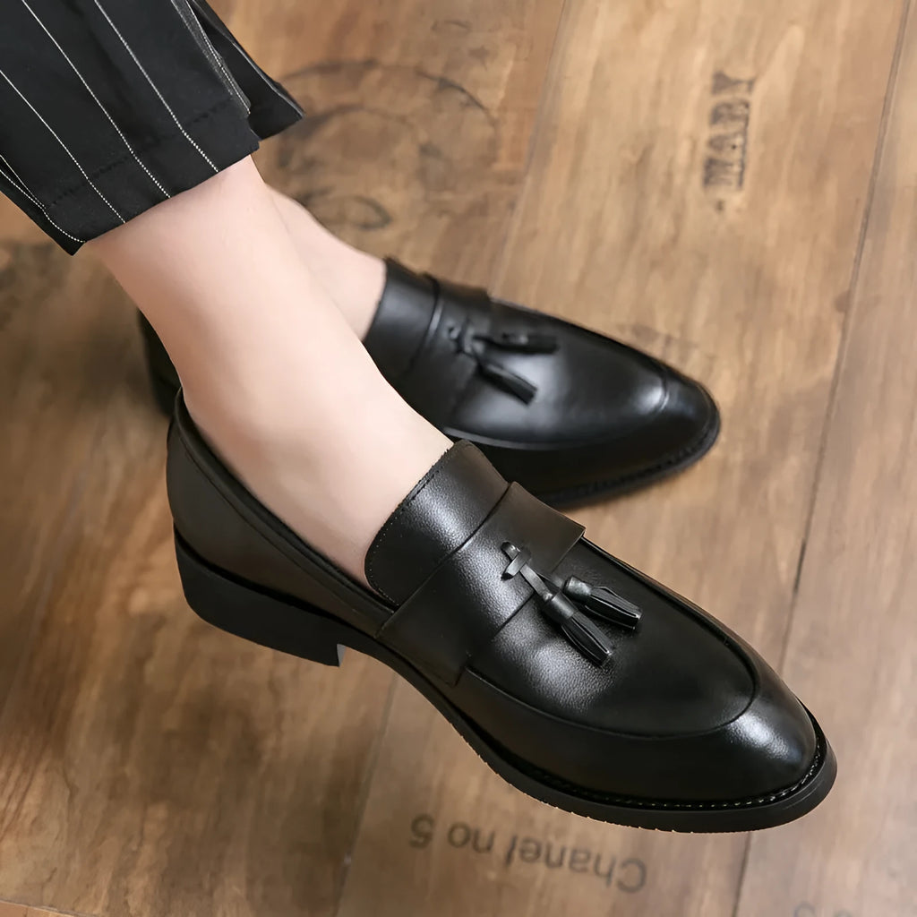 Men's black and brown slip-on business casual shoes with tassel detail and rubber sole.