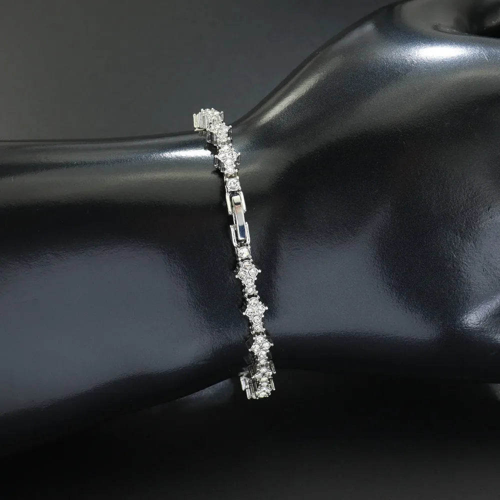 Flower-shaped cross tennis chain bracelet in gold alloy on white background showing diamond and geometric detailing