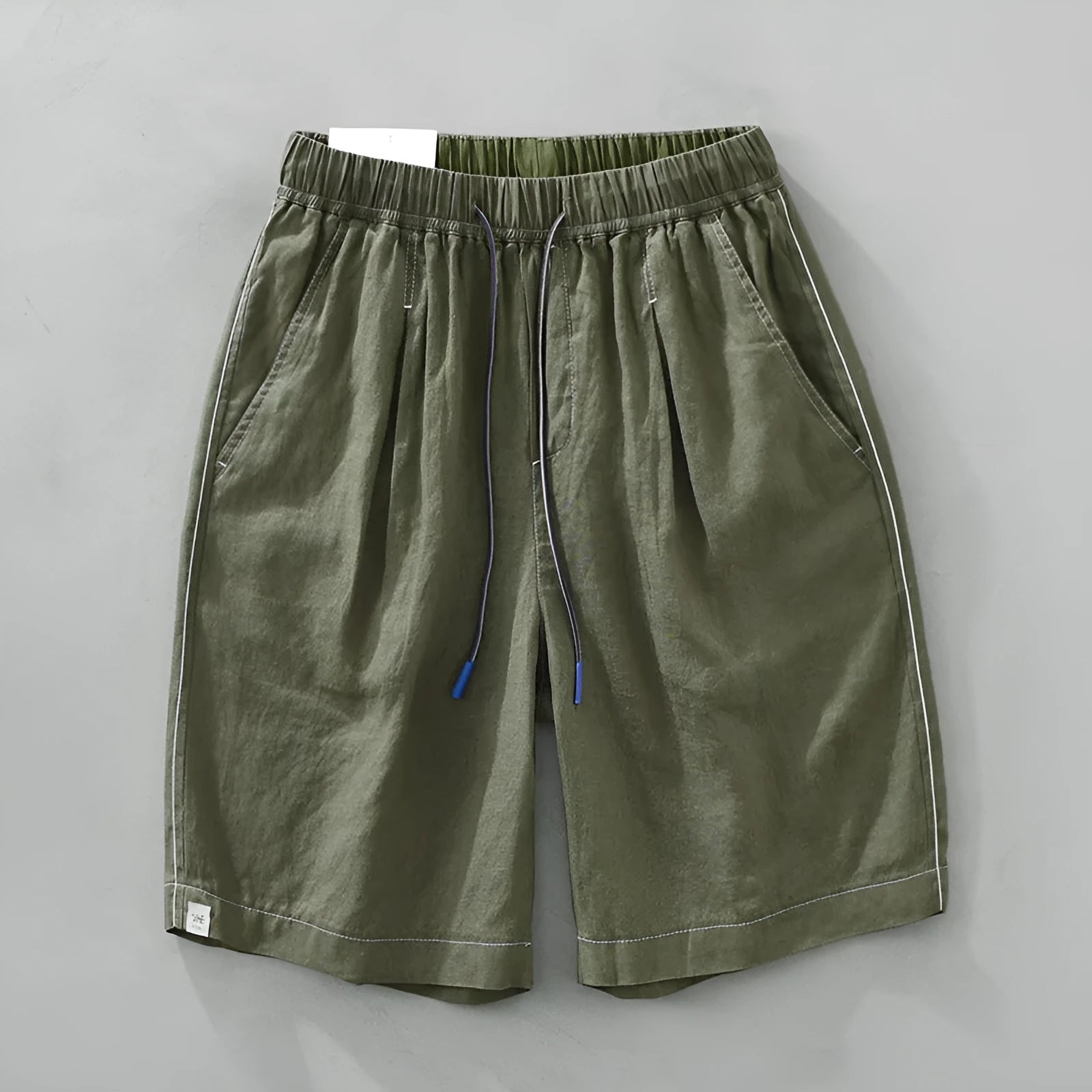 Man wearing green linen drooping shorts with a drawstring waist and mid-calf length.