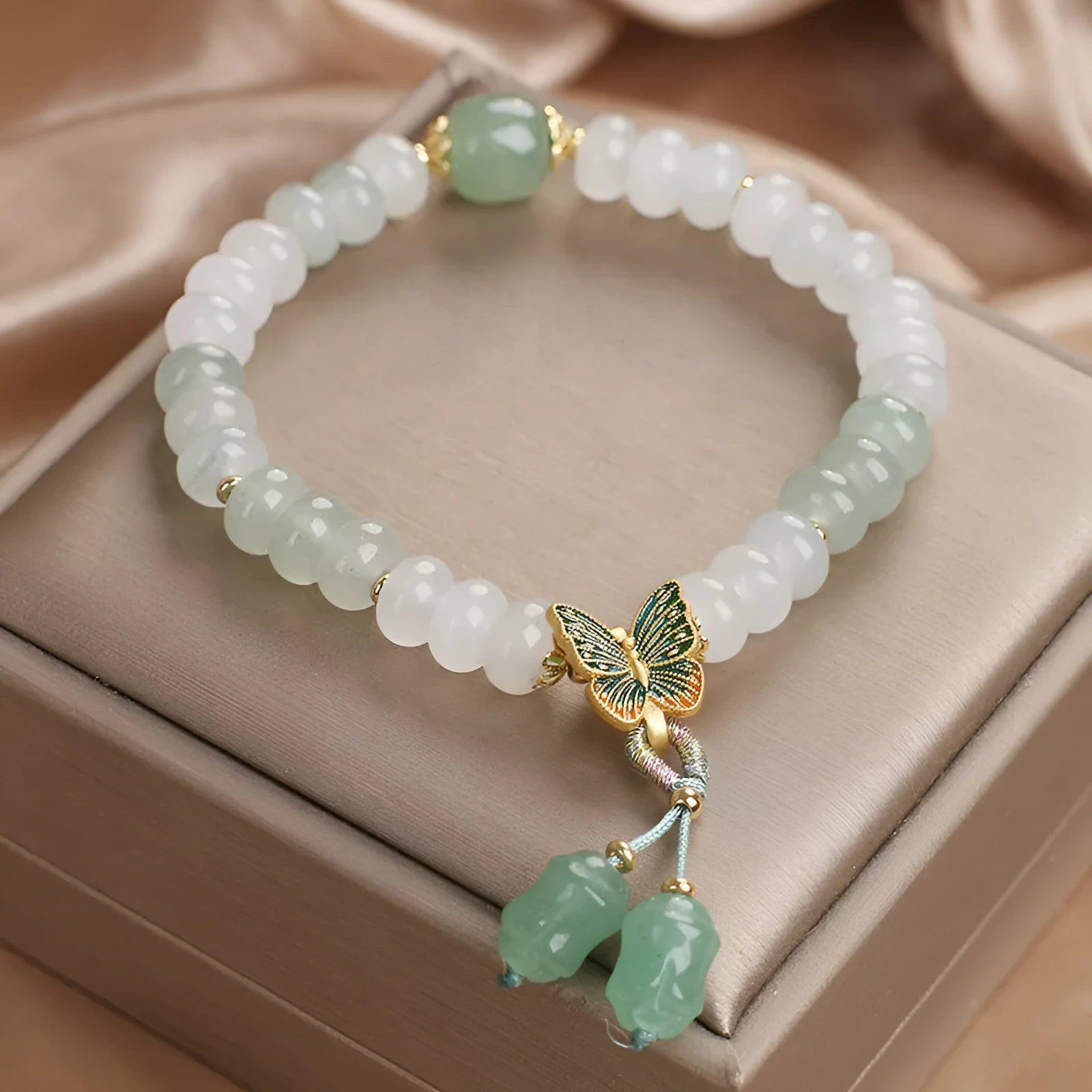 Green crystal abacus bead bracelet with a retro butterfly charm and tassels on a white background.