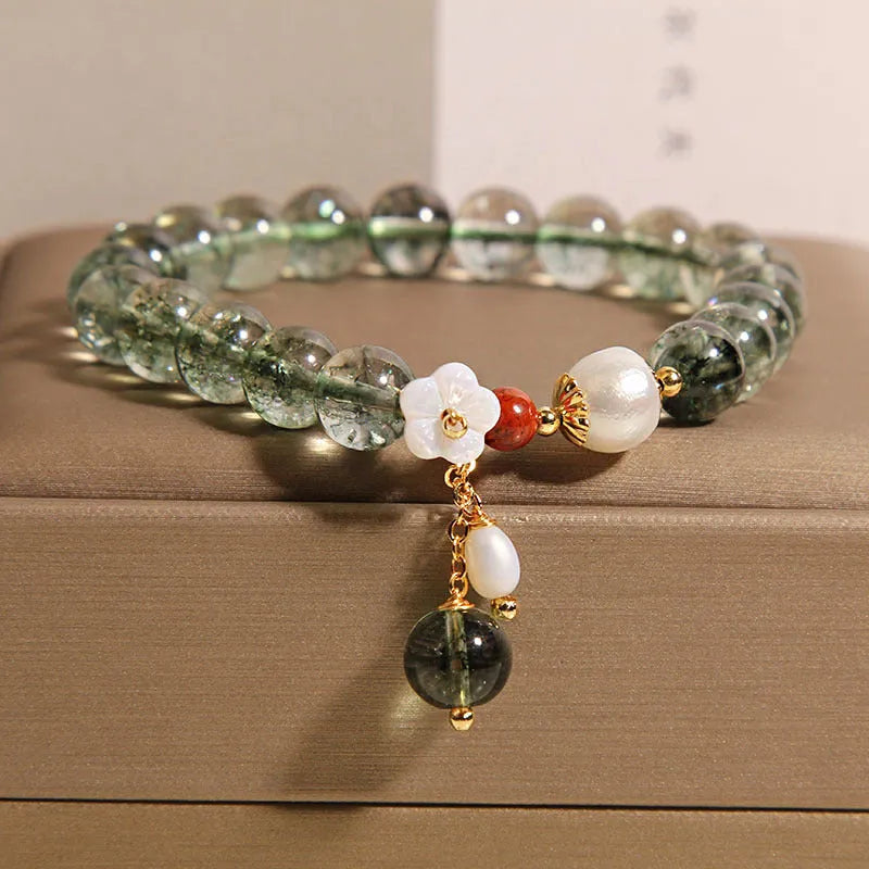 Green phantom quartz crystal bracelet with a silver shell flower charm on a model's wrist.