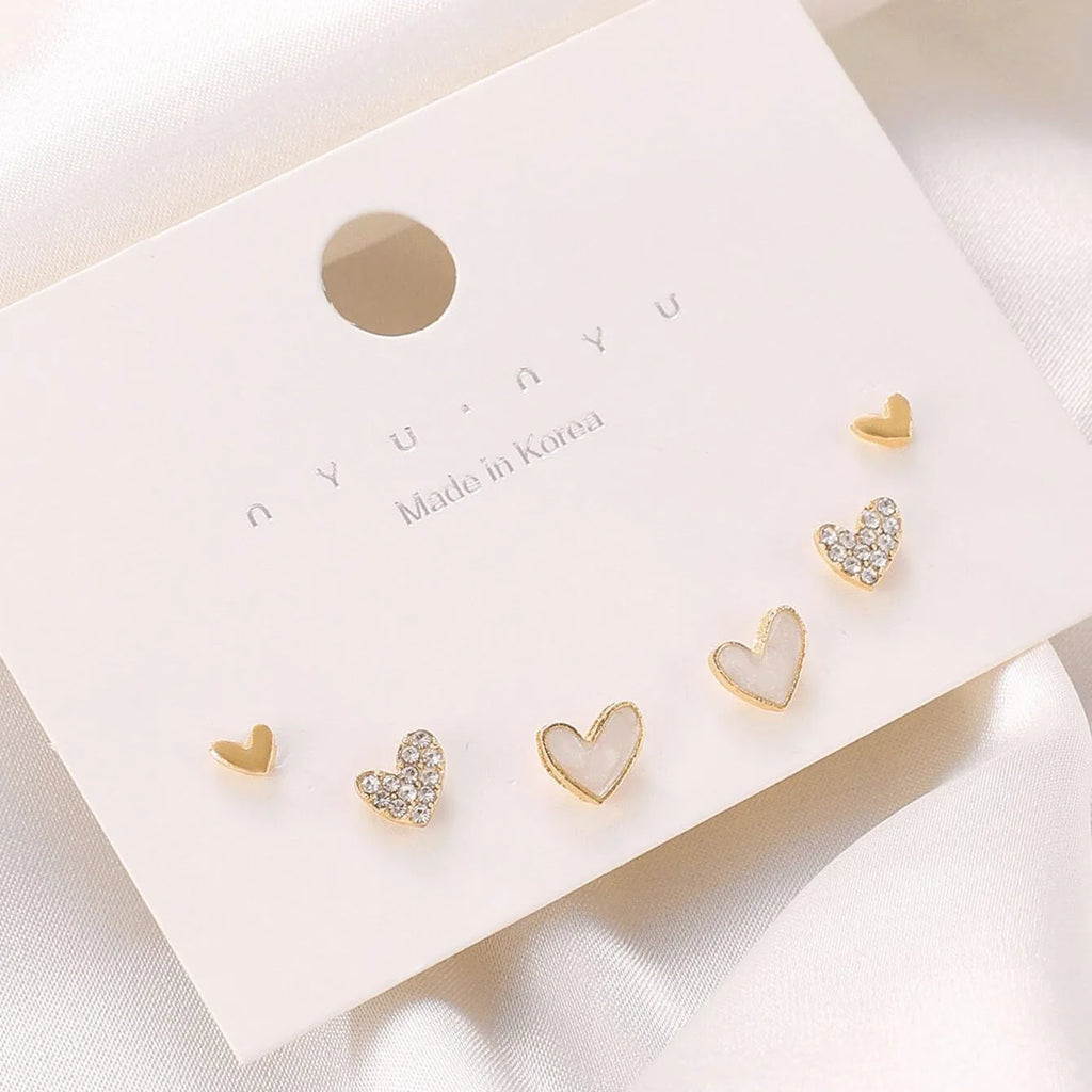Set of three pairs of heart-shaped alloy earrings in gold, black, white, and pink colours.