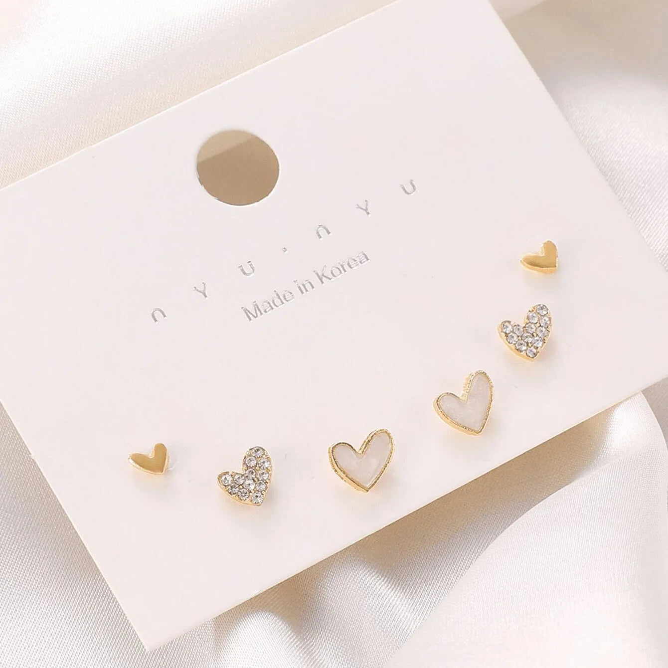 Set of three pairs of heart-shaped alloy earrings in gold, black, white, and pink colours.