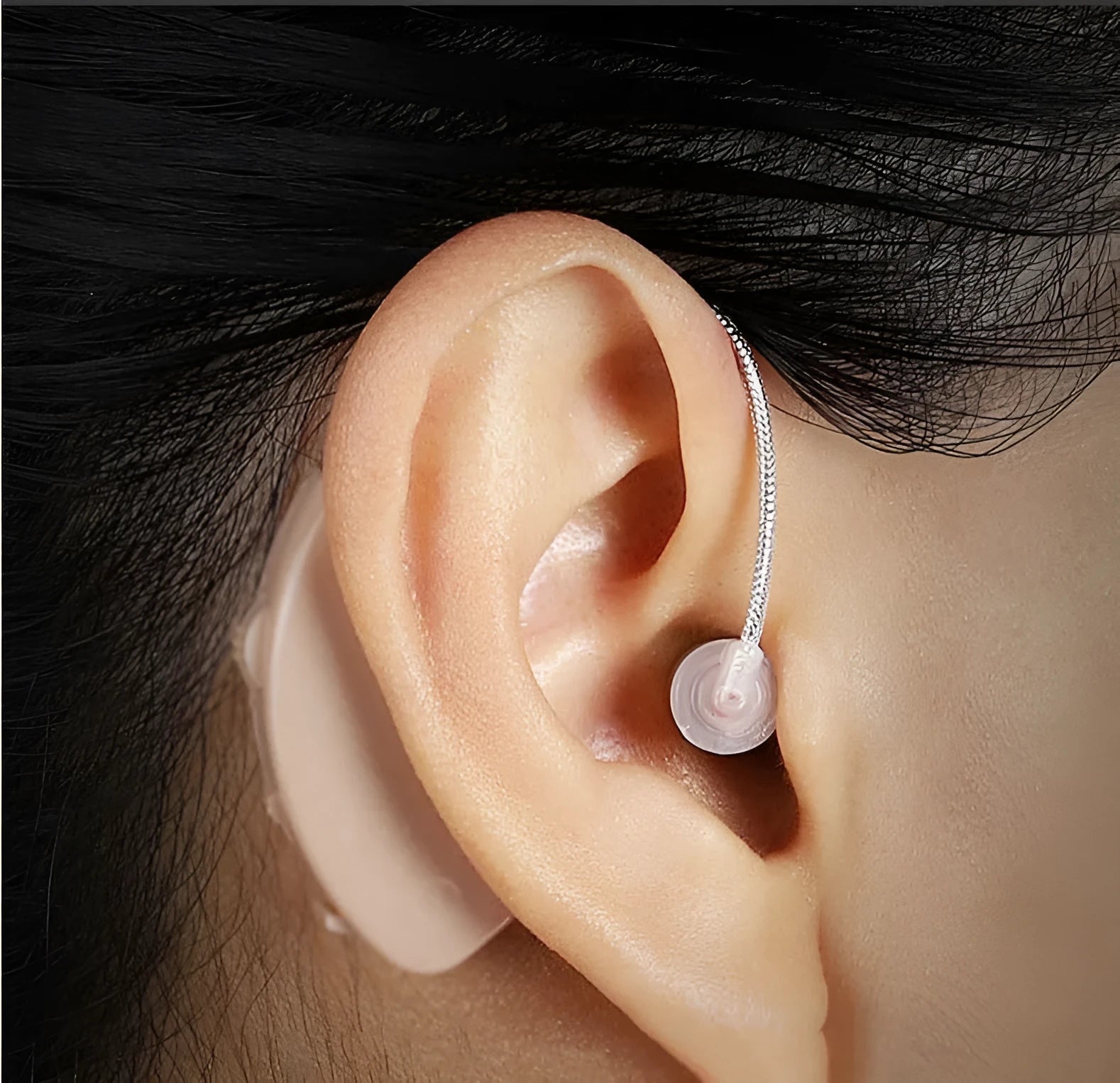 Black silicone rechargeable hearing aid amplifier for elderly users on a charging cable.