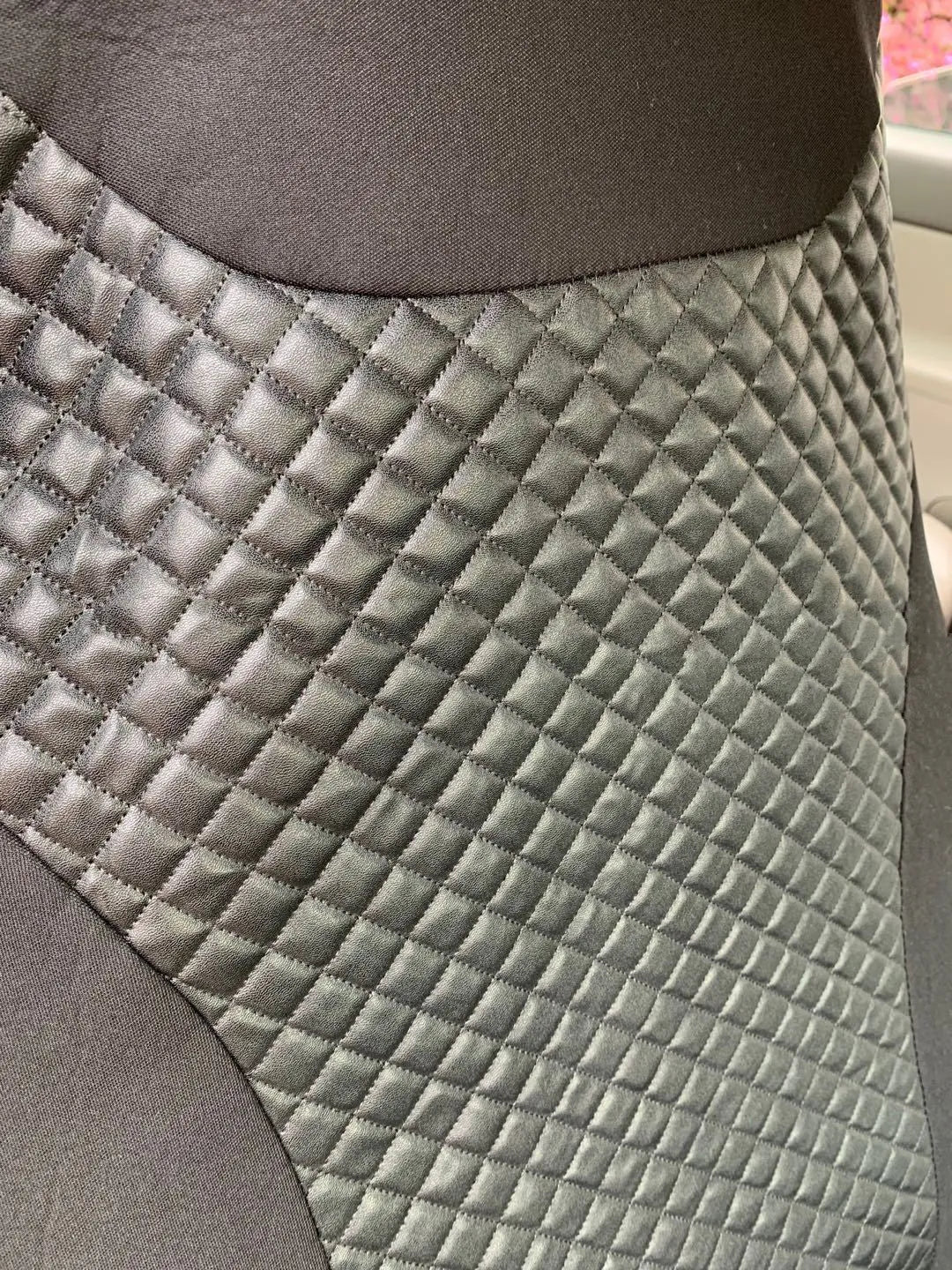 Black quilted automotive seat cover made of PU and polyester with plastic hooks.