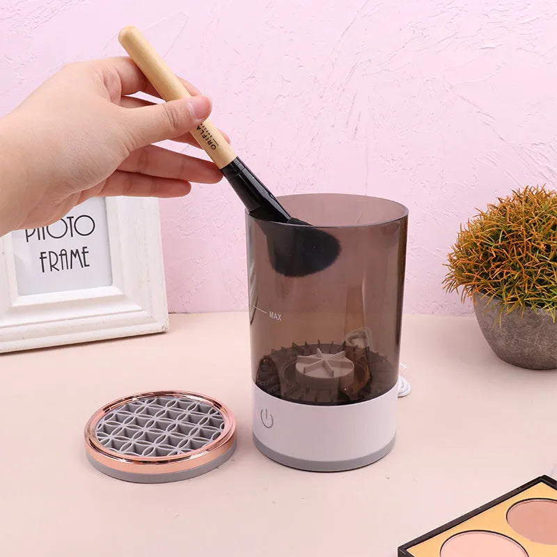 Grey and white electric makeup brush cleaner machine with USB cable on a white background