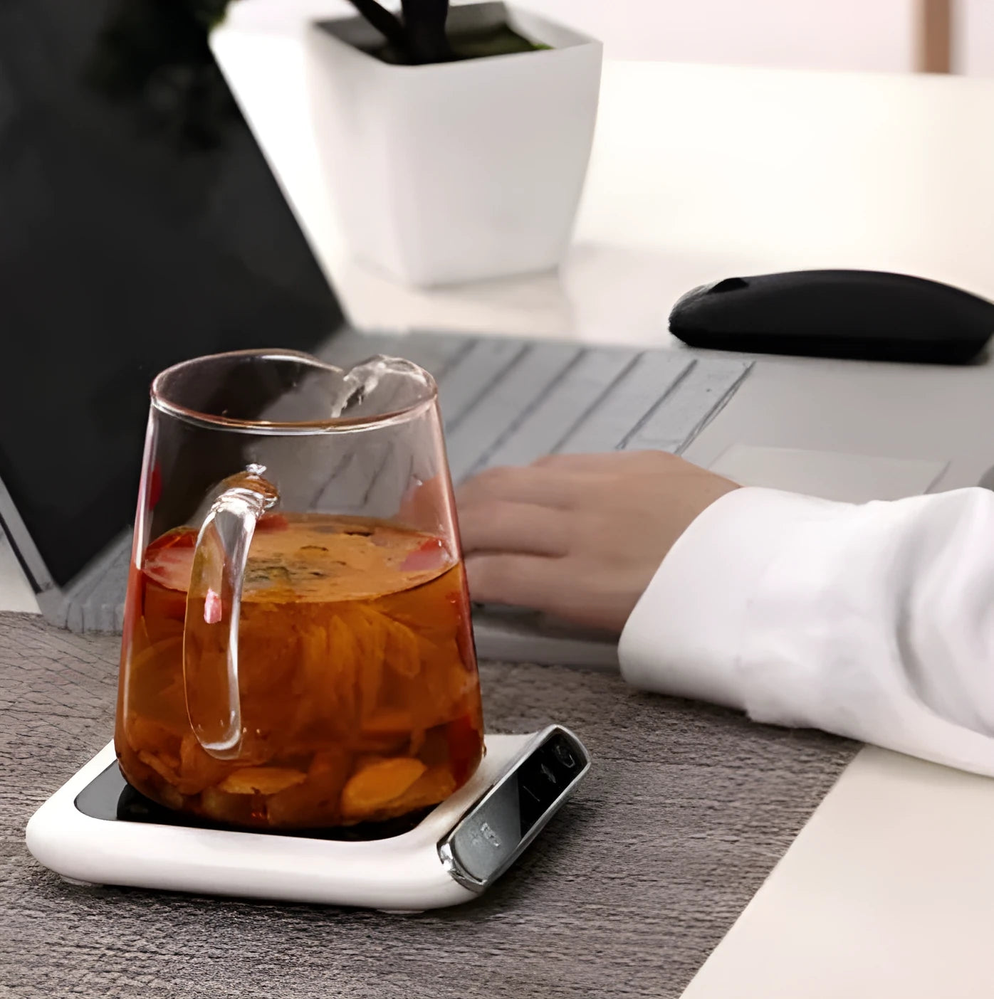 Black USB cup warmer on a desk next to a coffee mug, showing control panel.