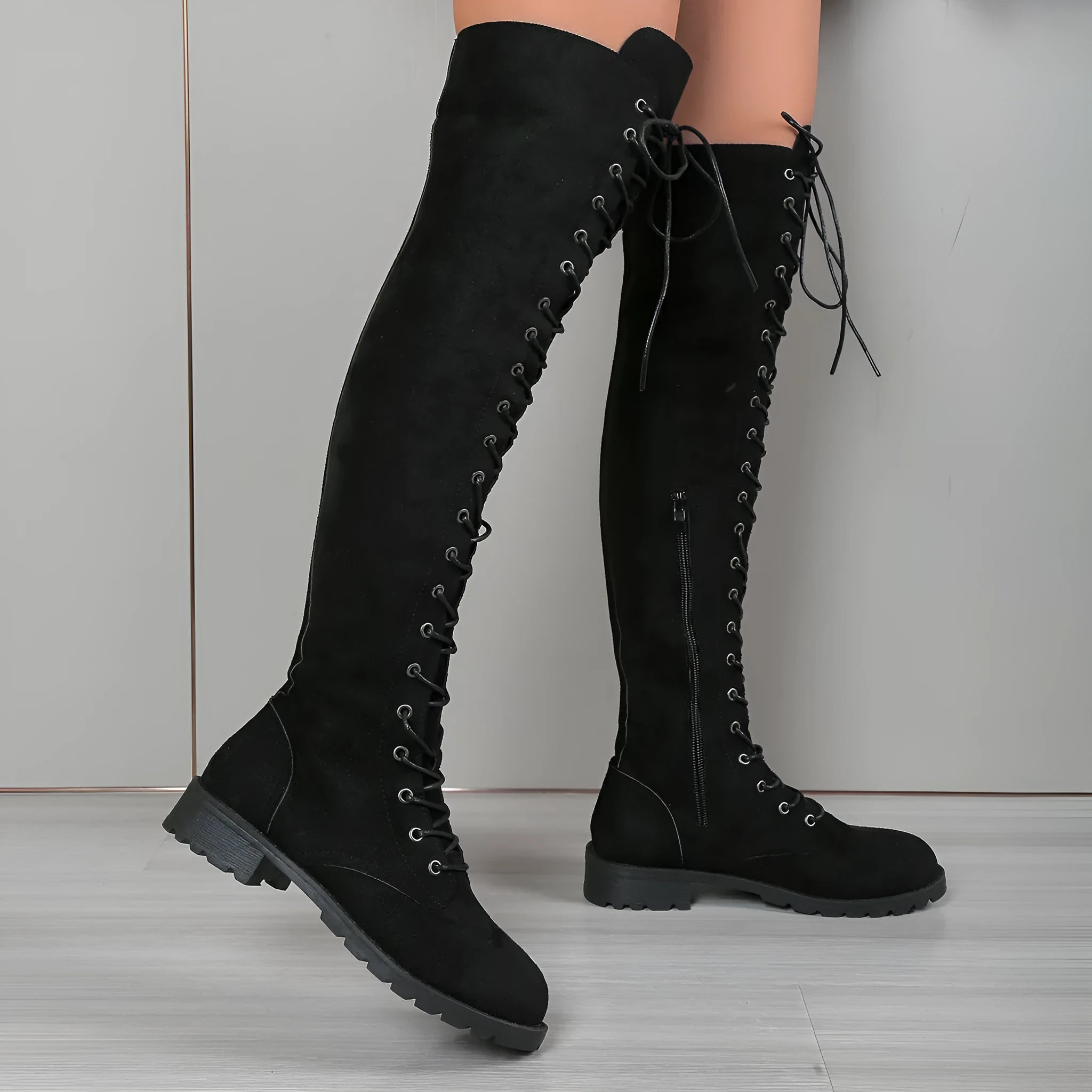 Black lace-up over the knee women's boots with a round toe and flat rubber sole on a plain background.