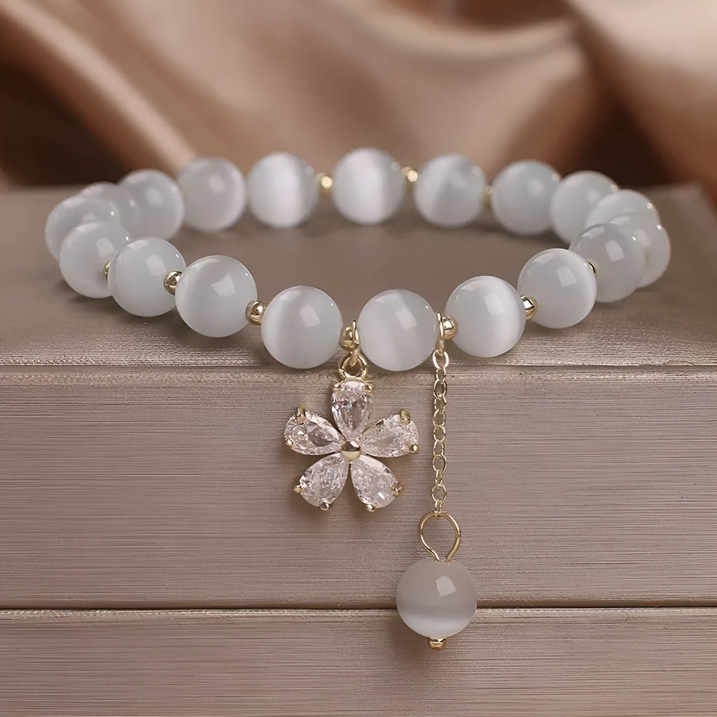 White cat's eye stone bracelet with small flower charms, tassel pendant, and safety buckle clasp.
