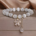 White cat's eye stone bracelet with small flower charms, tassel pendant, and safety buckle clasp.